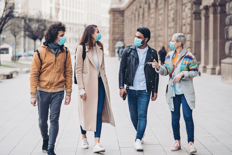 Four friends wear masks as they stroll down the street together. 